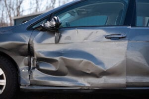 A car with its door open and the side of it dented.