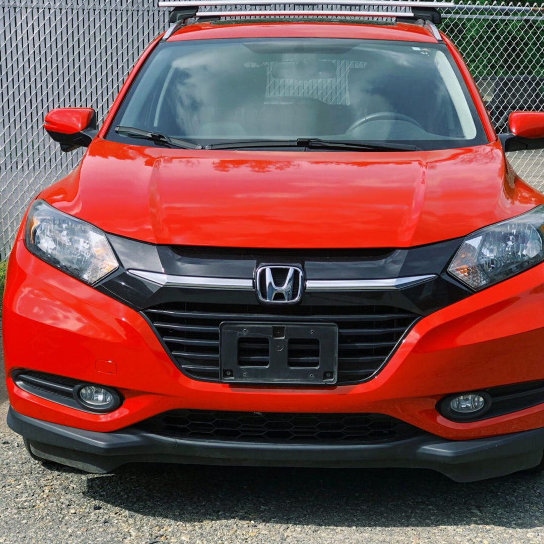 A red car parked in front of a fence.