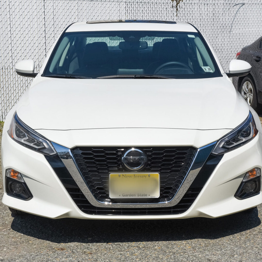 A white car parked in front of a fence.